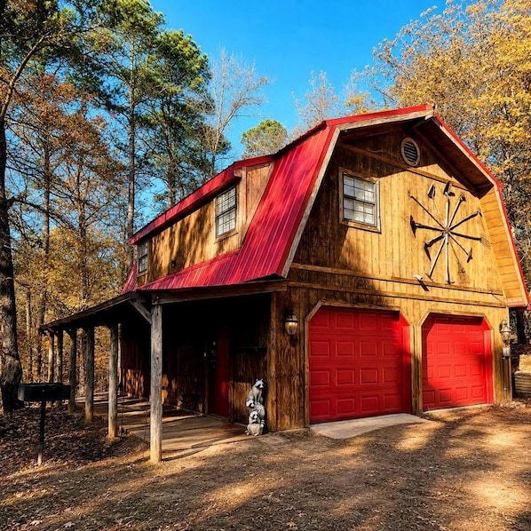 Un edificio de estilo rústico tipo granero, con techo rojo, revestimiento de madera y un garaje con puertas rojas.