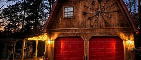 Une grange en bois avec deux portes de garage rouges, une fenêtre et un motif décoratif en forme d’étoile sur le mur.