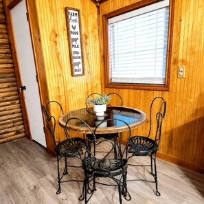 A wooden-paneled room with a round table and four chairs, a window with blinds, and a wall sign listing farm products. - Rustic Retreat near Lake O the Pines: Gorgeous Barn in Warlock, Texas (Warlock)