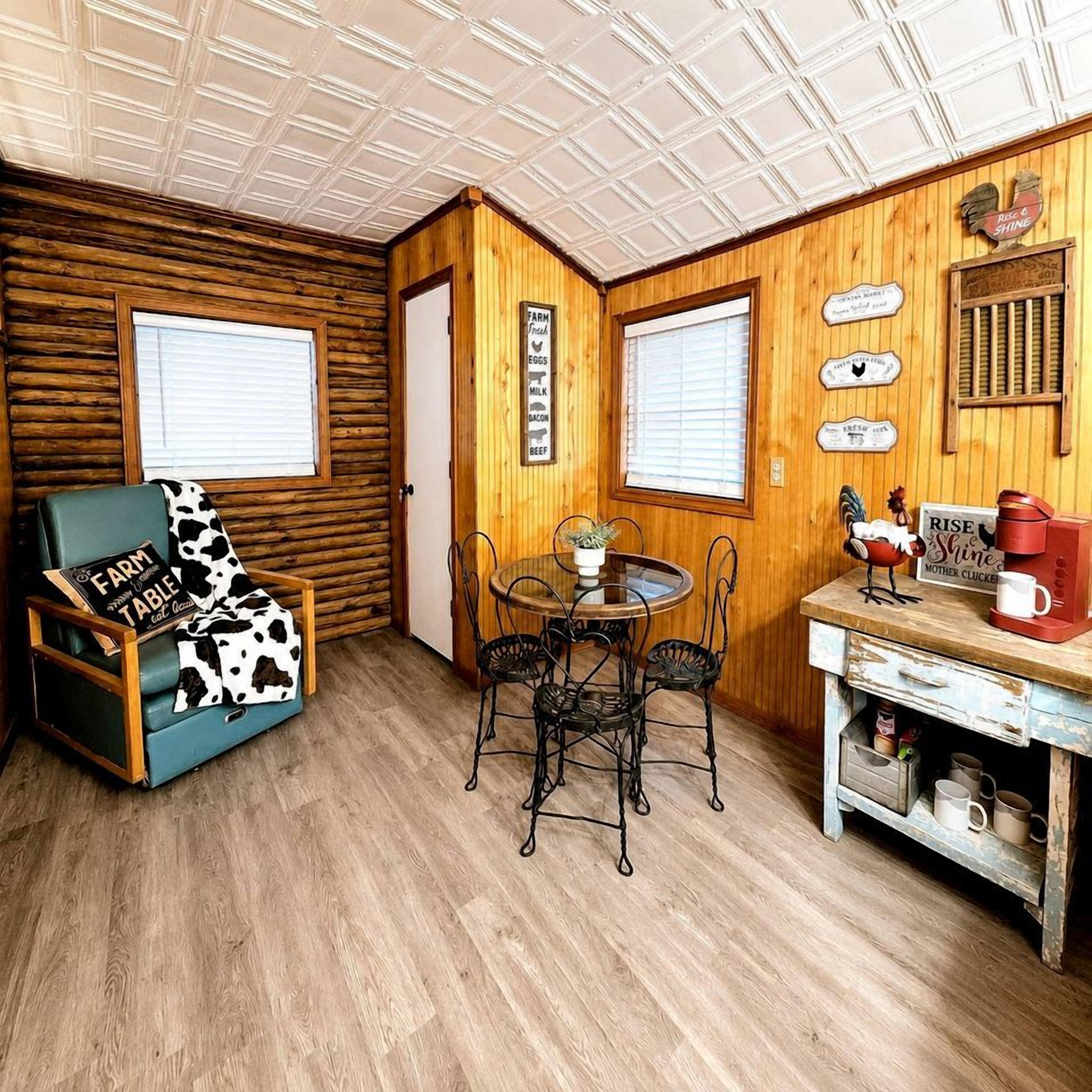 A cozy room with wooden walls, a dining table with chairs, a blue armchair, and a coffee station.