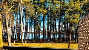 A hot tub surrounded by a wooden deck, with a view of a forest and a body of water in the background.