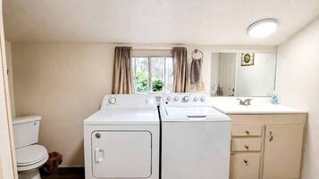 A compact bathroom with a toilet, two stacked washers, a sink, and a mirror.