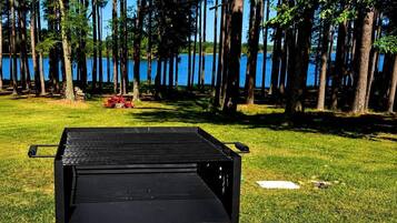 Un área de parrilla al aire libre con vista a un lago y árboles en el fondo.