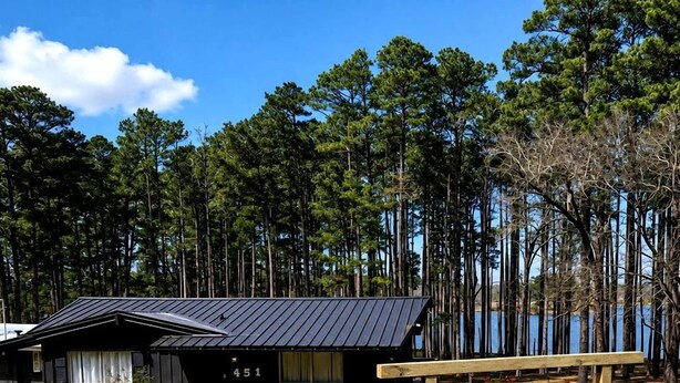 A cabin with a metal roof, numbered 451, surrounded by a gravel area and a sign indicating 'KNOTTY PINE'.