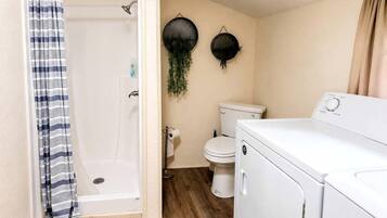 A compact bathroom with a shower, toilet, and a washing machine.