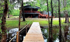 A wooden dock leading to a building with a red exterior, surrounded by trees and water. - Beautiful Rustic Wooden Cabin in Quitman, Mississippi (Quitman)