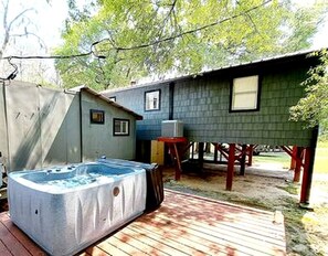 Un jacuzzi en una terraza de madera, un cobertizo pequeño y una casa con porche.