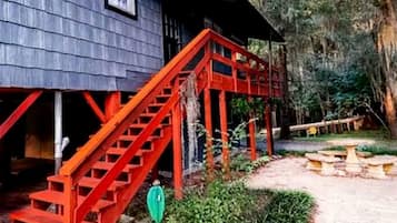 A rustic wooden house with a red staircase leading to a porch.