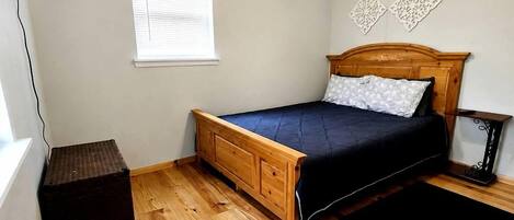 A bedroom with a wooden bed, a ceiling fan, a window with blinds, and a small table.