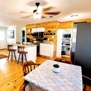 A kitchen with wooden cabinets, a microwave, and a refrigerator. There is a dining area with a table and chairs.