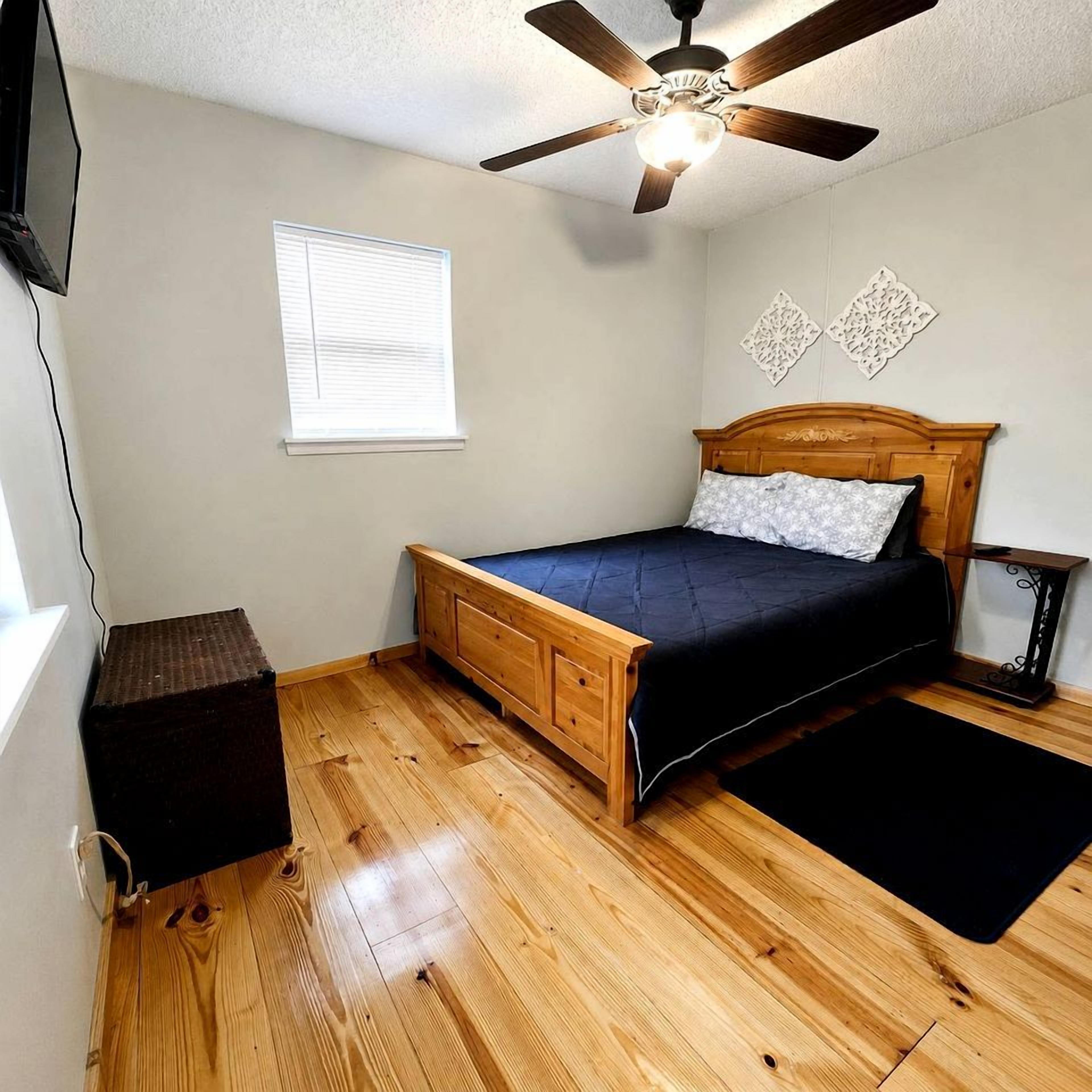 A bedroom with a wooden bed, a ceiling fan, a window with blinds, and a small table.
