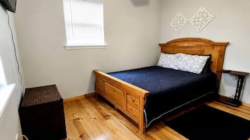 A bedroom with a wooden bed, a ceiling fan, a window with blinds, and a small table.
