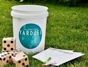 A white bucket labeled 'YARDZEE' with dice and a card on grass.