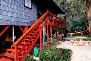 A rustic wooden house with a red staircase leading to a porch.