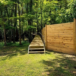 A wooden pathway leading into a forested area with a wooden fence on one side. - The Knee Knocker on Caddo Lake: Family Cabin near Karnack, Texas (Karnack)