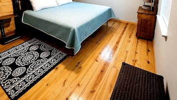 Una camera da letto con un letto, pareti in legno, una ventola a soffitto, una finestra con persiane e un piccolo armadietto di legno.