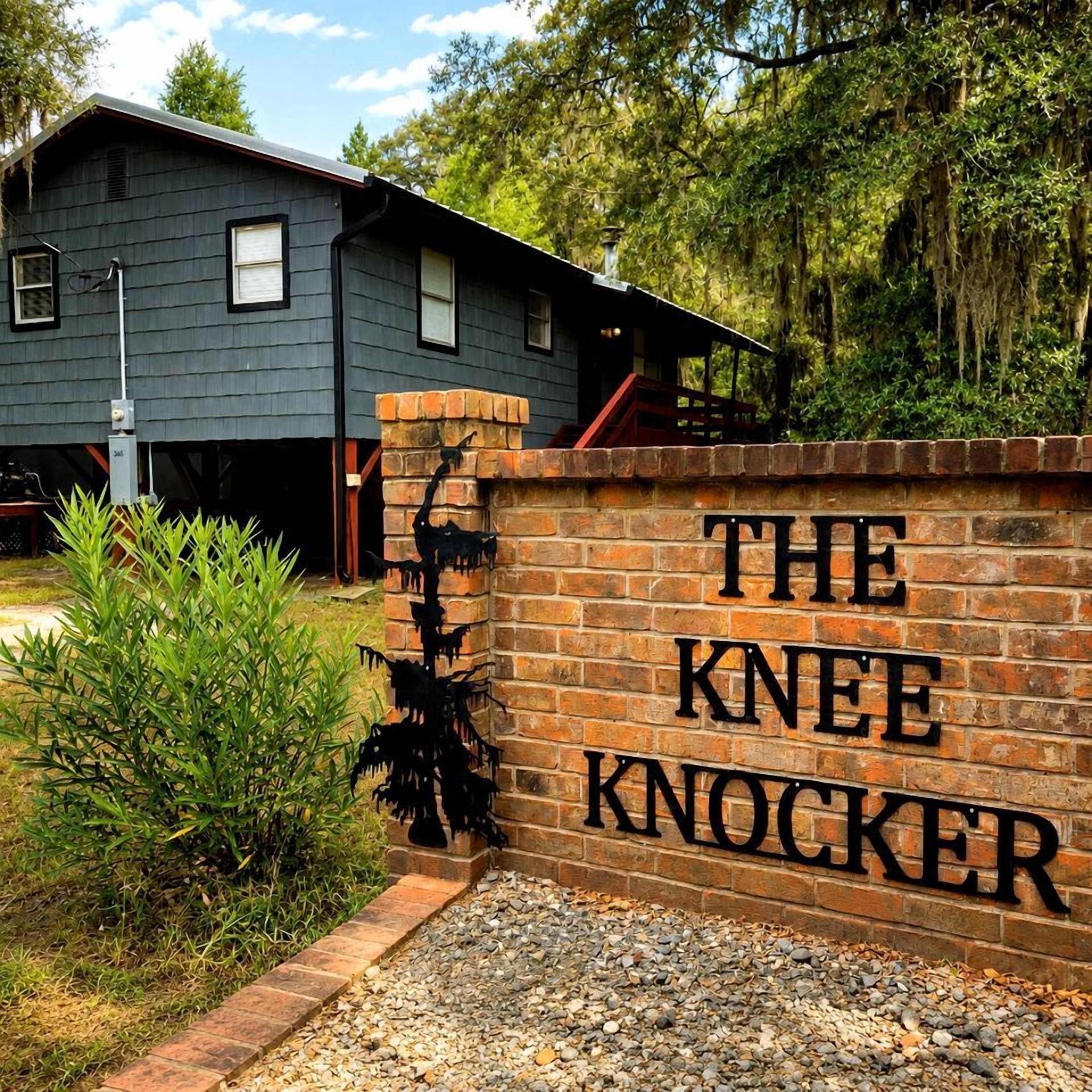 Un mur de briques sur lequel on peut lire l’inscription « THE KNEE KNOCKER », avec une maison en arrière-plan.