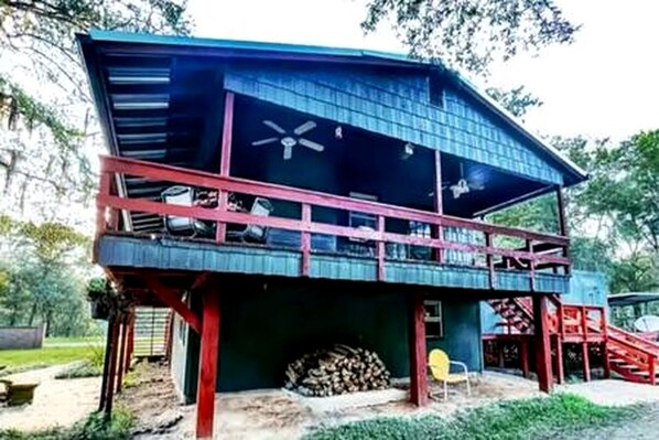 A two-story house with a balcony, a ceiling fan, and a stack of firewood.