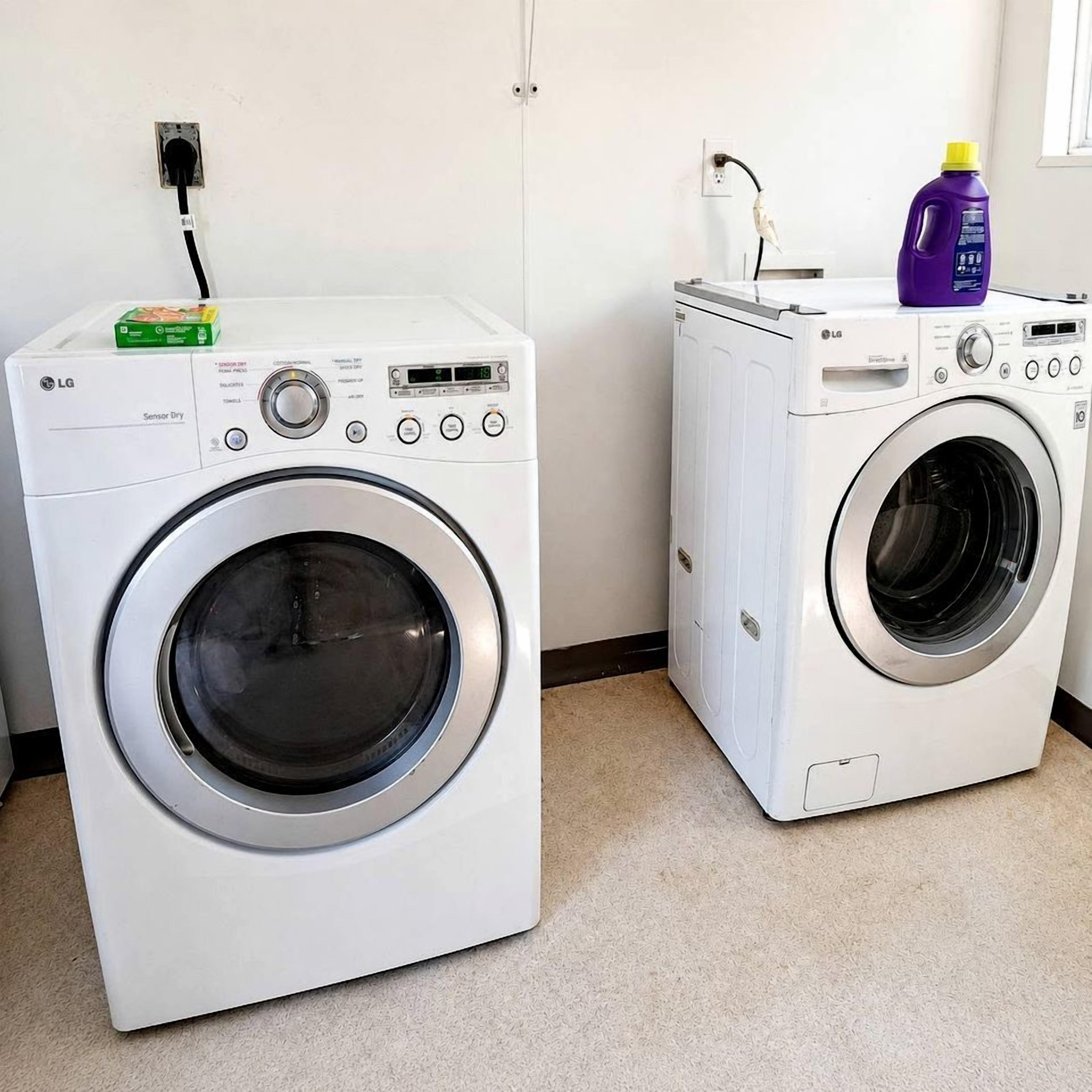 Two front-loading washing machines in a laundry room with a power outlet and a window.