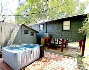 A hot tub on a wooden deck, a small shed, and a house with a porch.