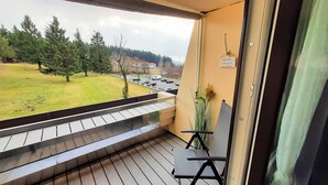Een balkon met uitzicht op een gazon en geparkeerde auto's.