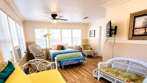 A room with a bed, two chairs, a white sofa, a ceiling fan, and a television on the wall.