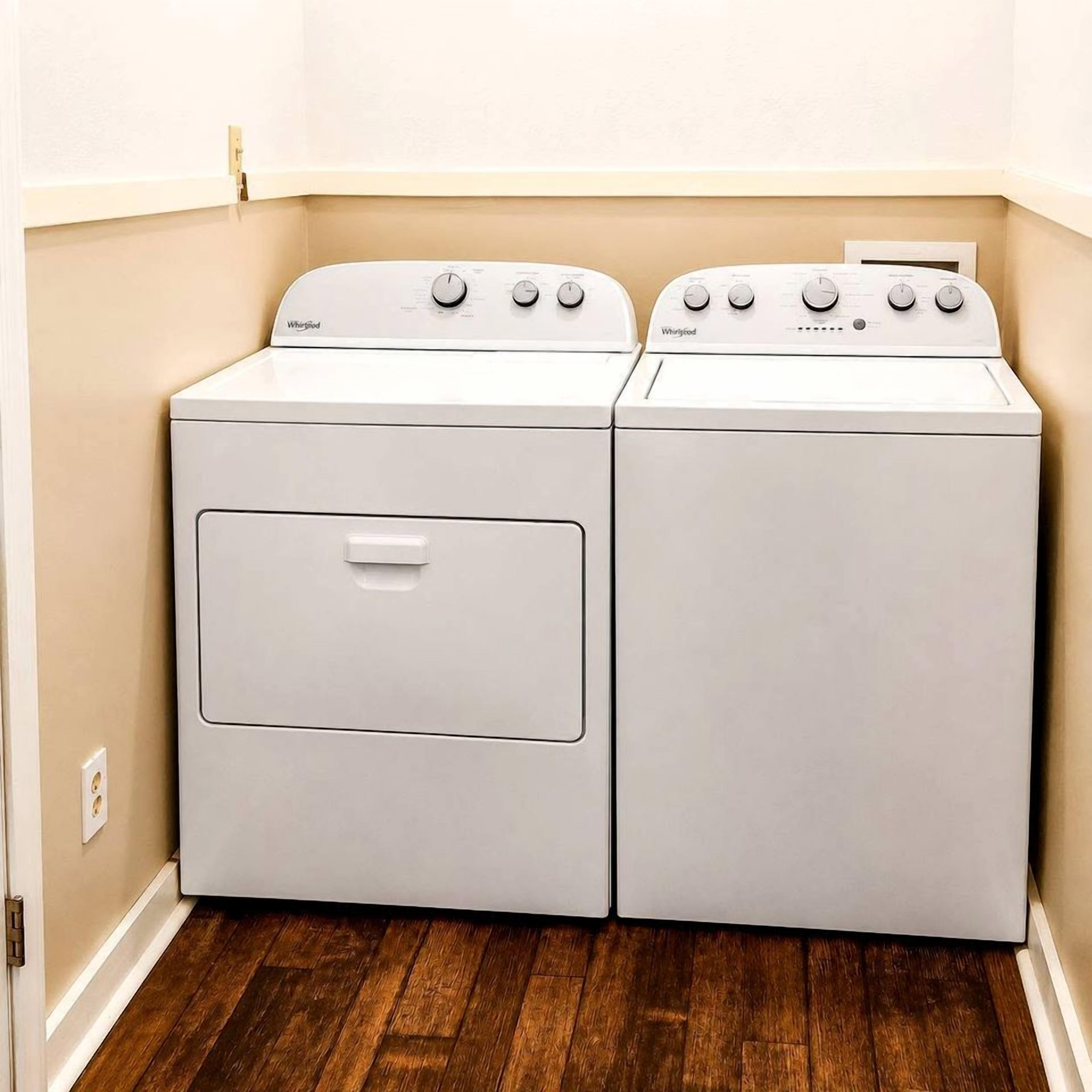 Une buanderie équipée de deux lave-linge et deux sèche-linge Whirlpool blancs, avec un plancher en bois et un mur de couleur beige.