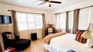 A bedroom with a bed, a desk, a chair, a ceiling fan, and a television.