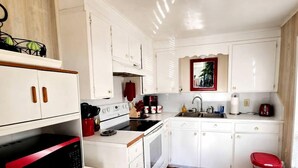 A compact kitchen with white cabinetry, a red microwave, and a wooden floor.