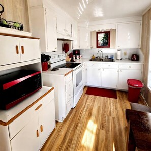 Una cocina compacta con muebles blancos, un microondas rojo y piso de madera.