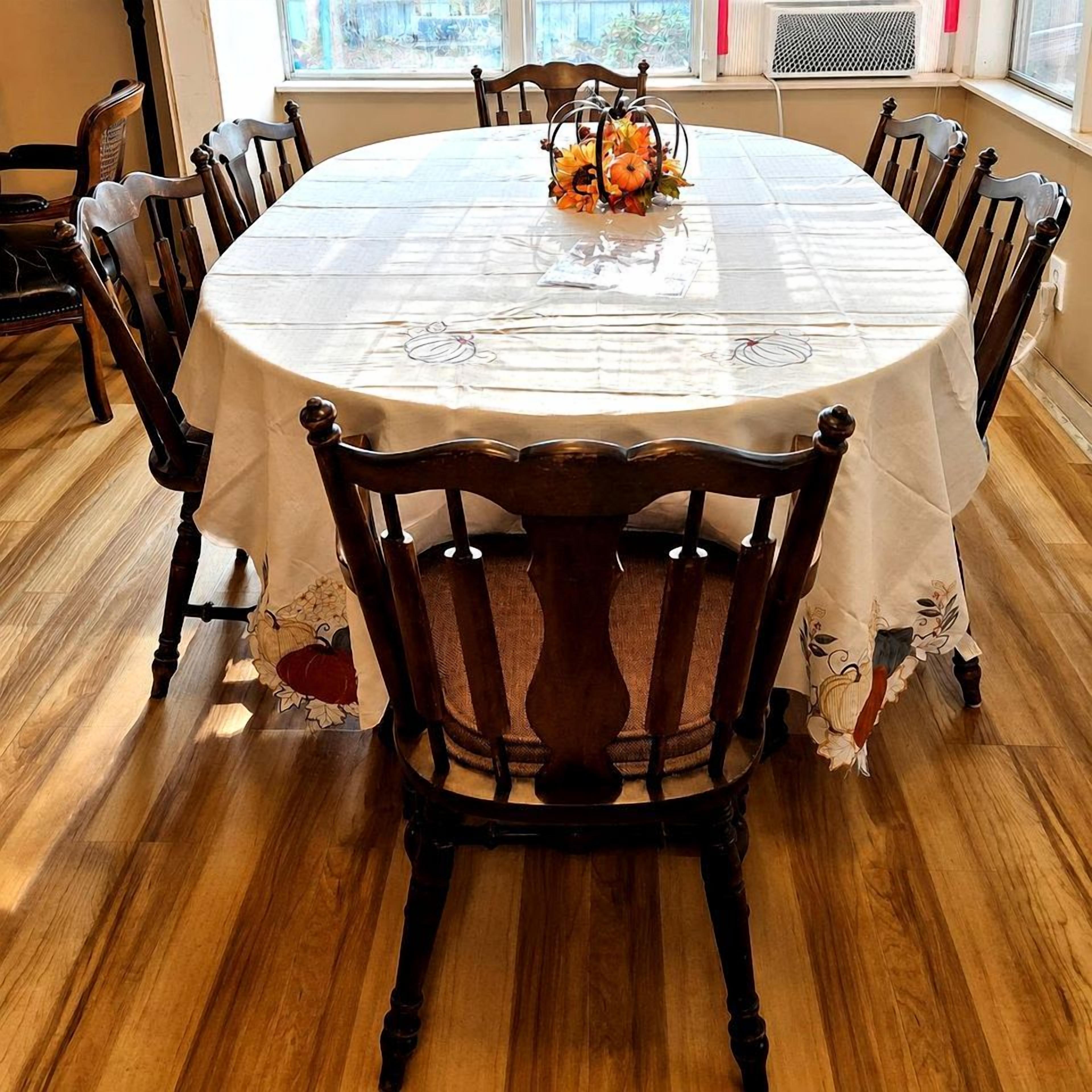 Une table de salle à manger ronde, recouverte d’une nappe blanche, entourée de chaises en bois ornées de motifs floraux.