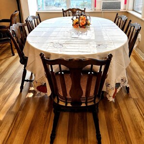 A round dining table with a white tablecloth, surrounded by wooden chairs with floral patterns.