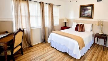 Een slaapkamer met een bed, een bureau, een stoel, een plafondventilator en een raam met gordijnen.