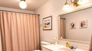 A bathroom with a toilet, sink, vanity, and a shower curtain.