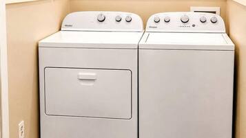 A laundry room with two white Whirlpool washers and dryers, wooden flooring, and a beige wall.