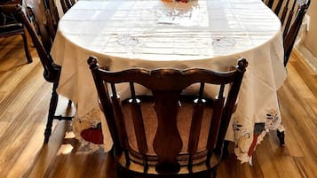 Een ronde eettafel met een witte tafelkleed, omringd door houten stoelen met bloemenmotieven.
