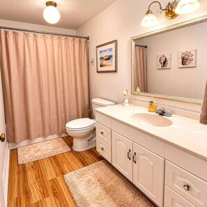 A bathroom with a toilet, sink, vanity, and a shower curtain.