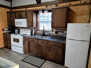 A kitchen with wooden cabinets, a white stove, a microwave, a sink, and a refrigerator.