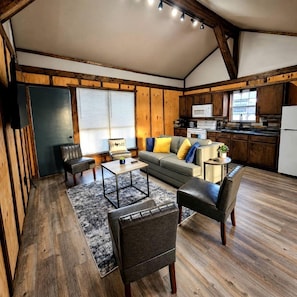 A spacious living area with a sofa, chairs, a coffee table, and a kitchen in the background.
