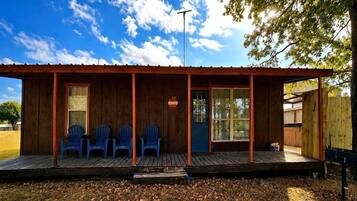 A small building with a porch, three blue chairs, and a blue door.