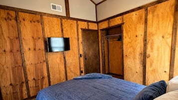 Een slaapkamer met een houten wandpaneel, een plafondventilator, een flatscreen televisie en een bed met blauw beddengoed.