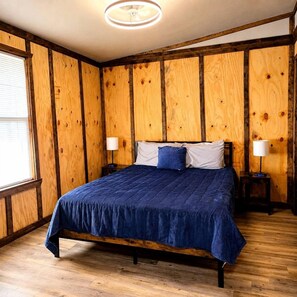 Ein Zimmer mit einer Holzpaneelausstattung, einem Bett mit blauer Bettdecke, zwei Nachttischlampen und einer Deckenleuchte.
