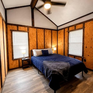 Ein Schlafzimmer mit einem Bett, zwei Nachttischen, einem Deckenventilator und Holzvertäfelung.