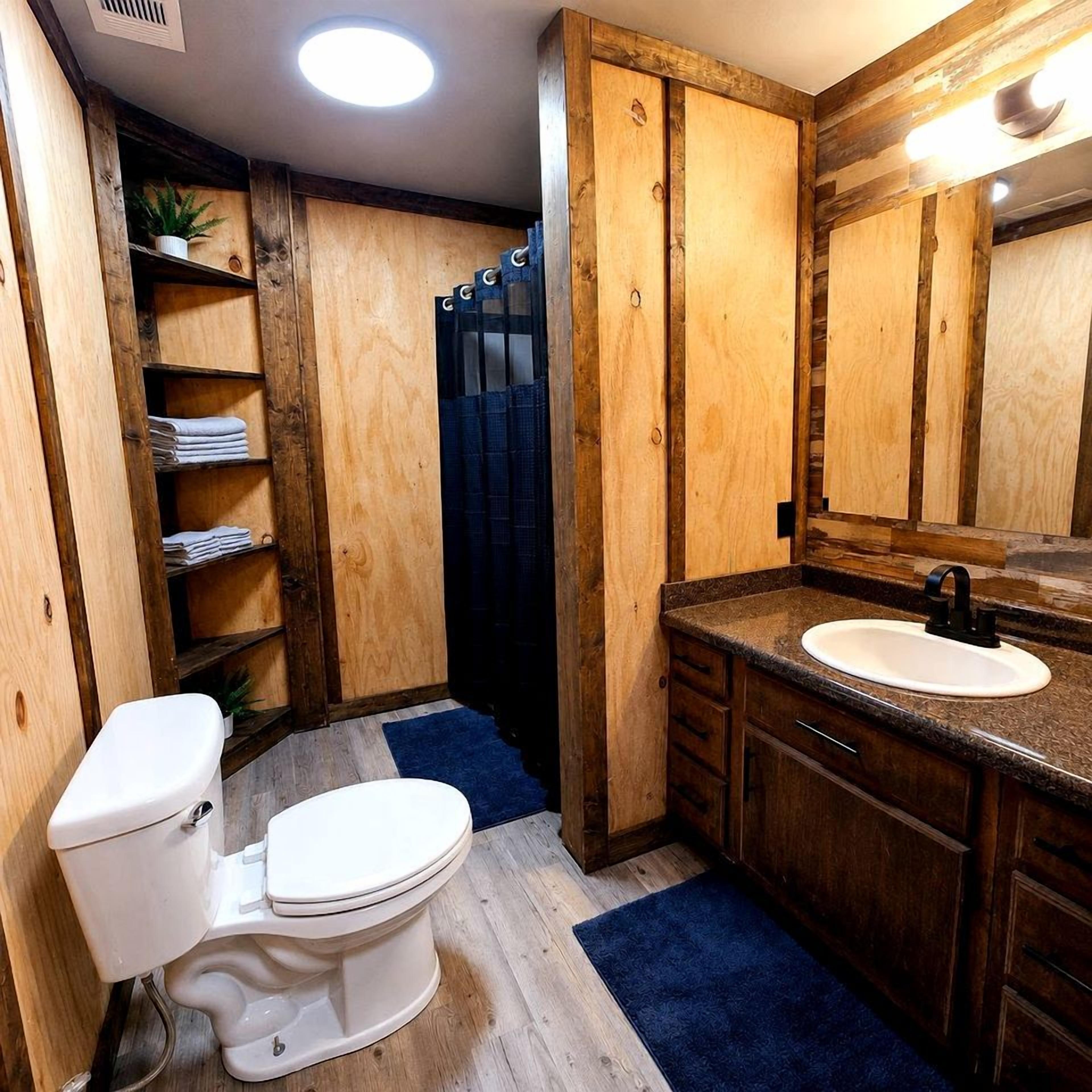 Une salle de bain avec des toilettes blanches, des meubles en bois, un lavabo avec un robinet noir et un rideau de douche bleu.