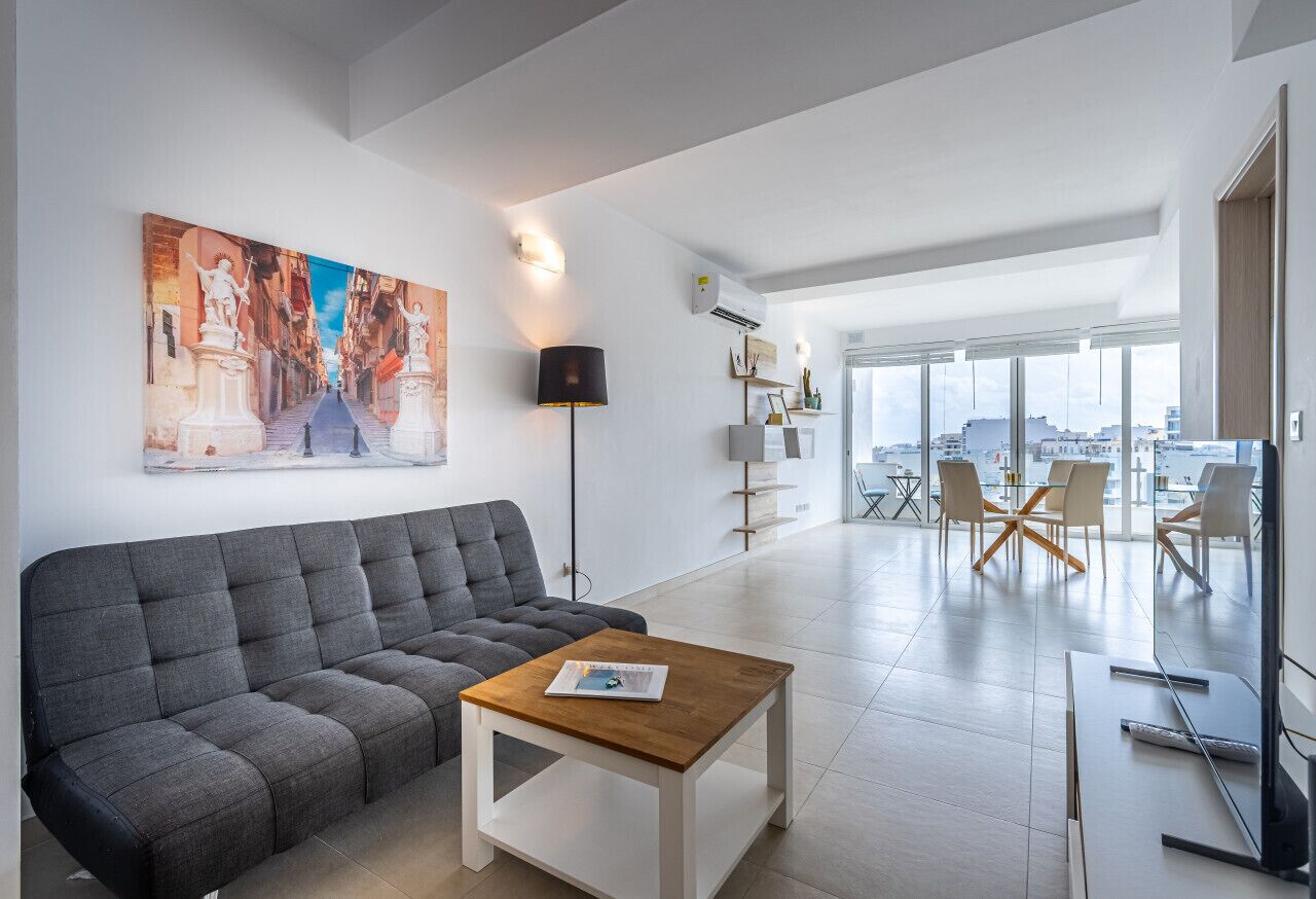 A modern living room with a grey sofa, a wooden coffee table, and a large painting of a street scene.