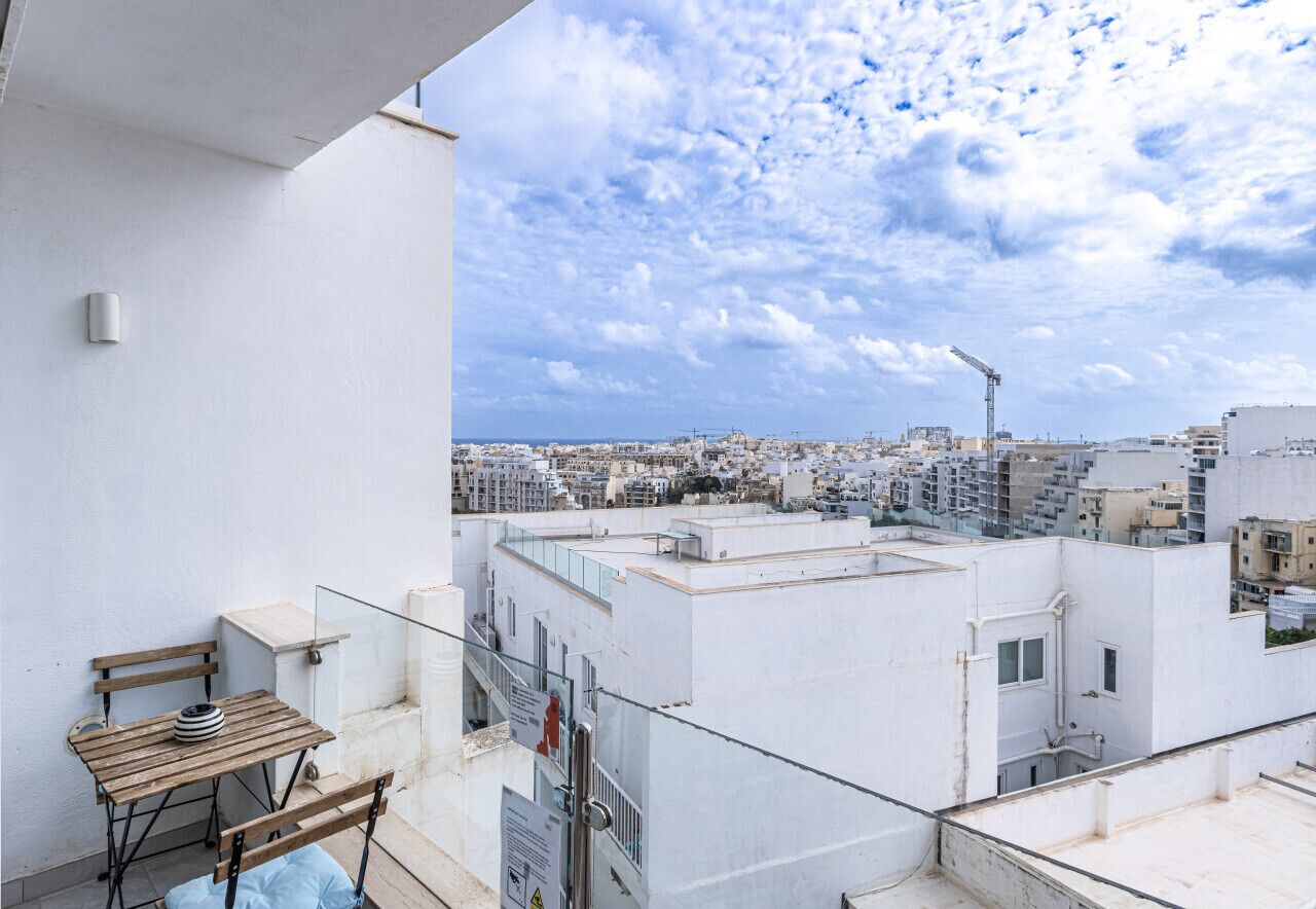 Terraza en la azotea con una mesa y sillas, con vistas a un paisaje urbano con edificios y una grúa.