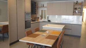 A modern kitchen with integrated appliances, a dining area with a table and chairs, and a view of the adjacent living space.