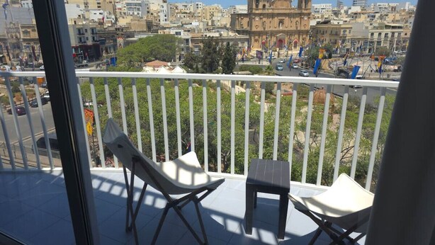 A balcony with two white chairs and a small table, overlooking a cityscape with historic buildings and a clear sky.