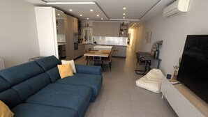 A modern living room with a sectional sofa, a dining area, and a kitchen in the background.