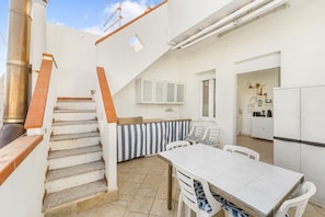 A kitchen with a white countertop, a dining table with chairs, a staircase with orange railings, and a white refrigerator.